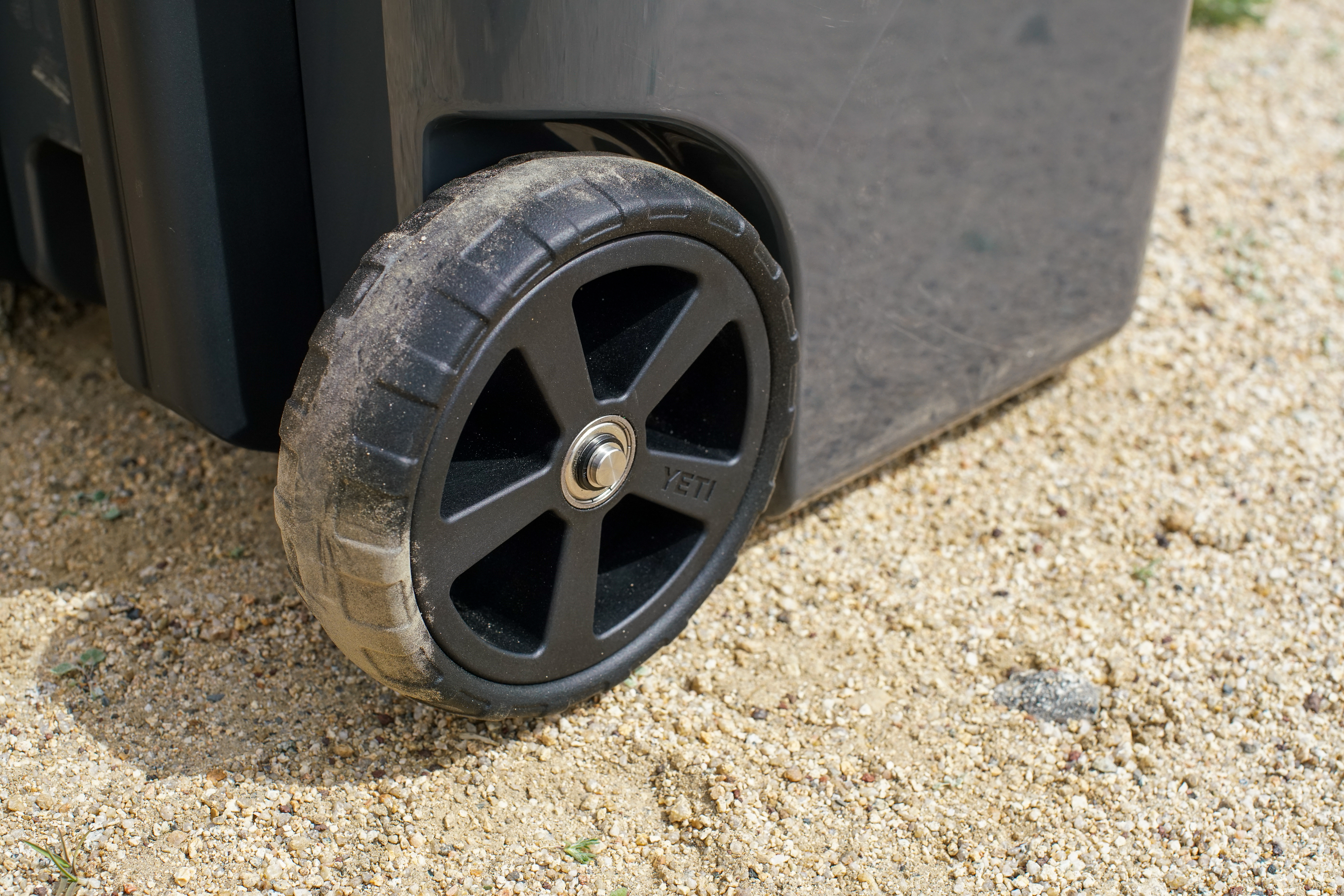 A close up of a single wheel on the YETI Roadie 48 cooler on a gravelly terrain. The wheel is dusty.