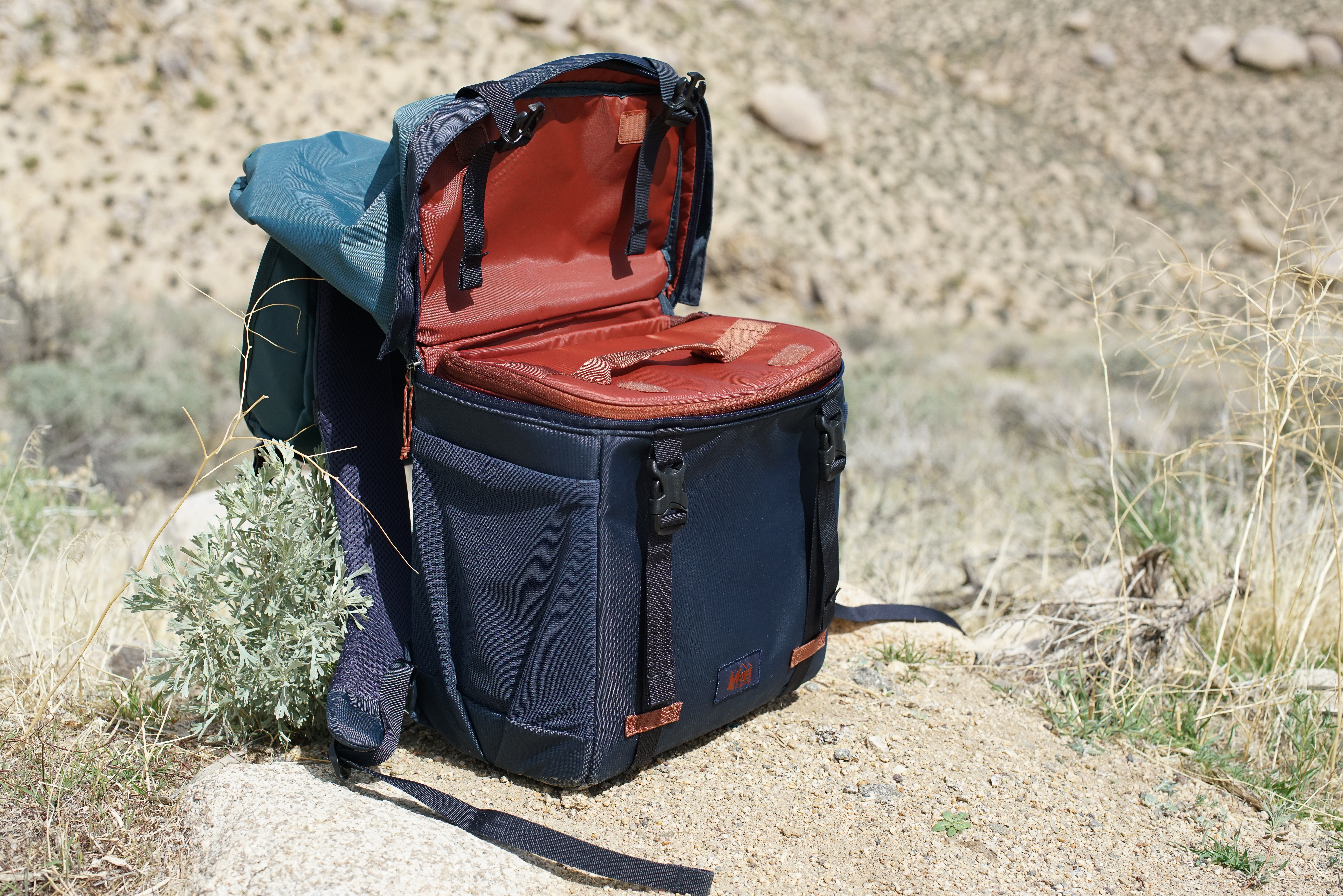 The REI Cool Trail Split Pack sits on the ground. The pack is zipped open from the middle and the cooler insert is visible.