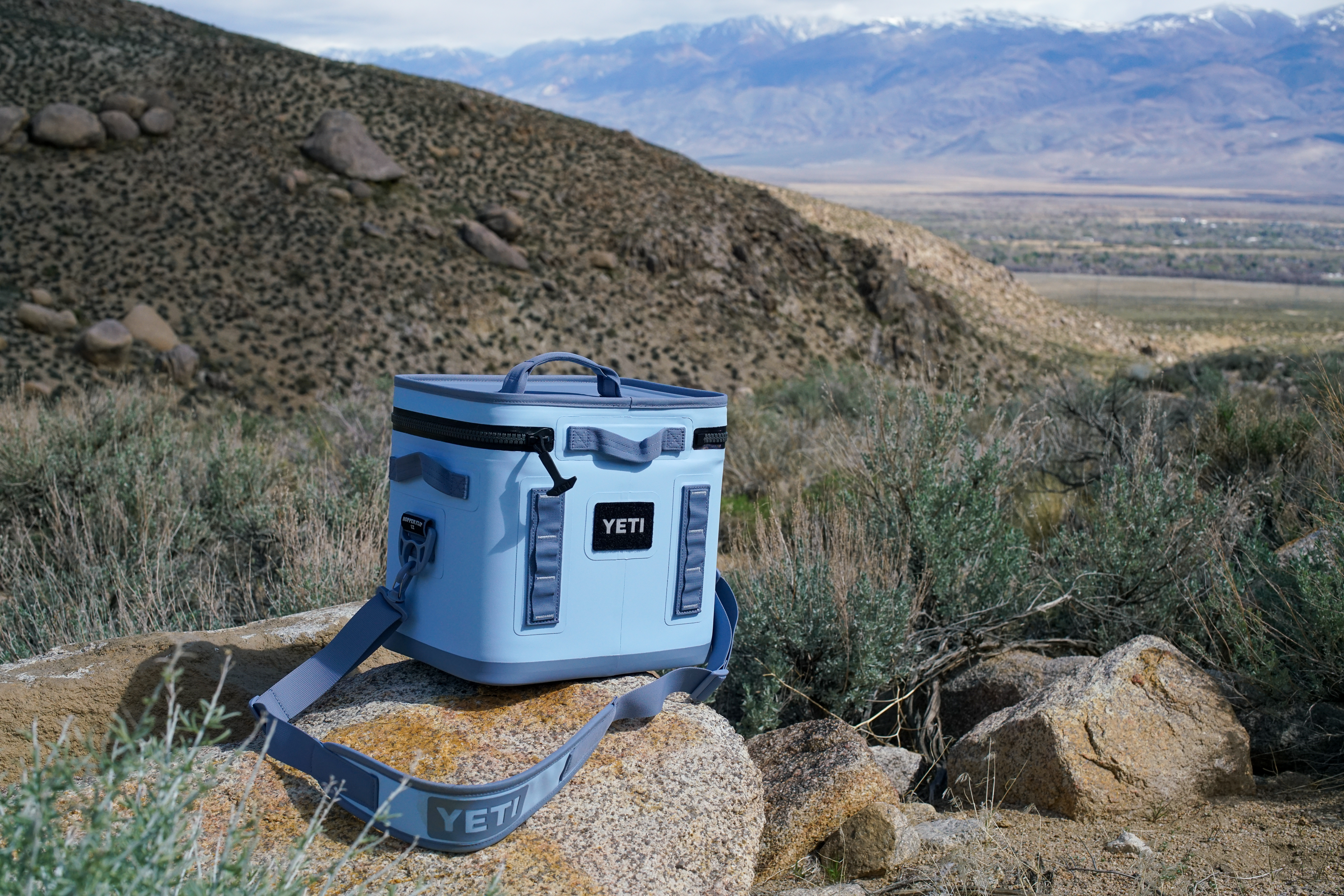 The YETI Hopper Flip 12 sits on a rock with sage brush and boulders in the background.