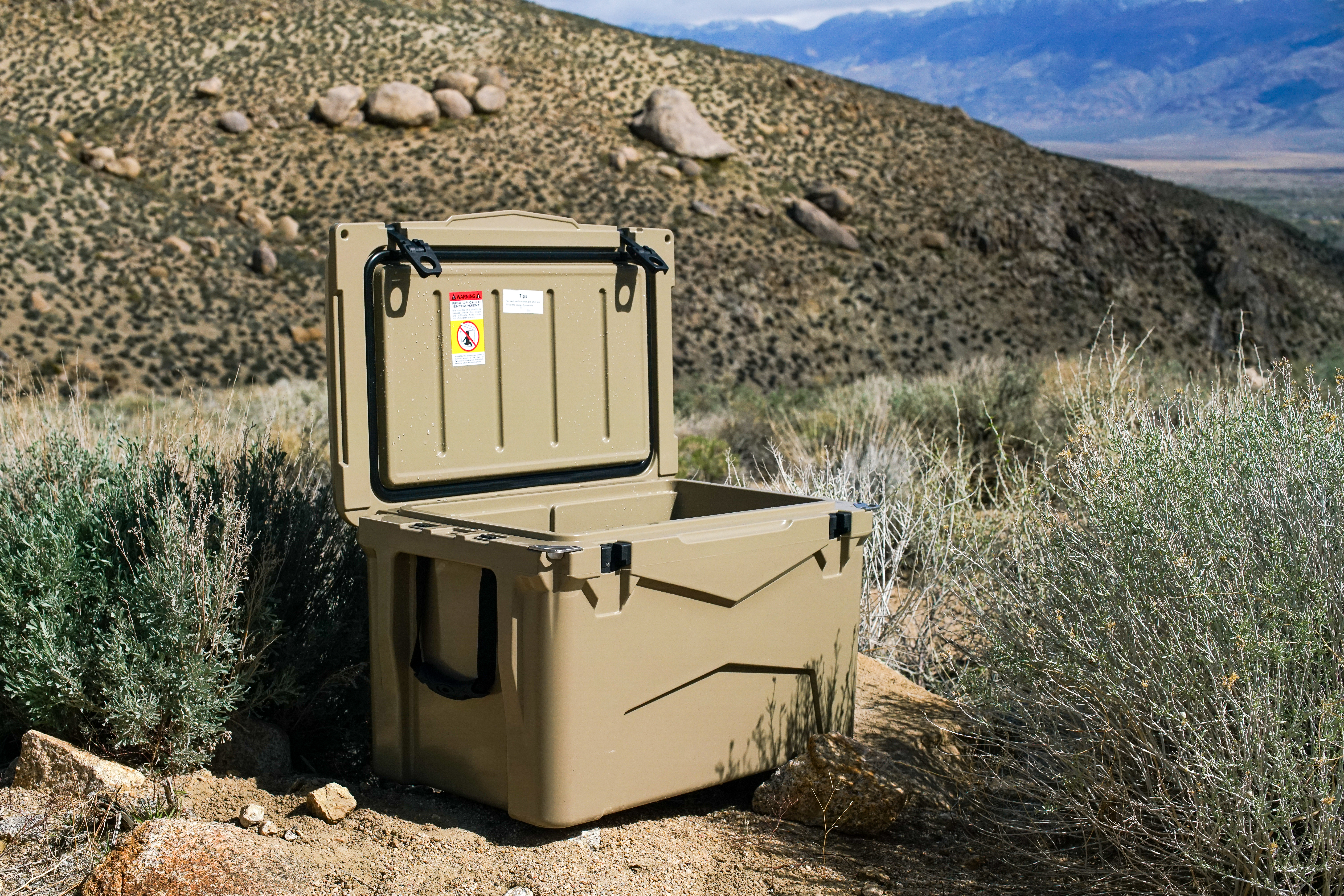 The XSpec 60QT cooler sits amongst sage brush with boulders in the background. The lid of the cooler is open.