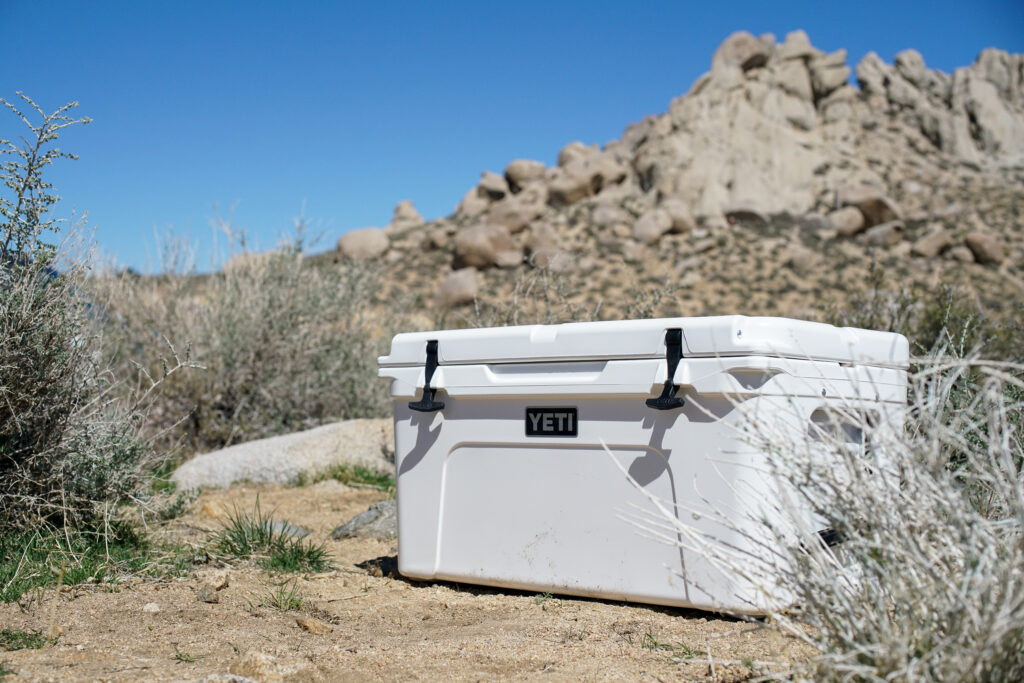 The YETI Tundra 65 sits on the ground with boulders in the background.