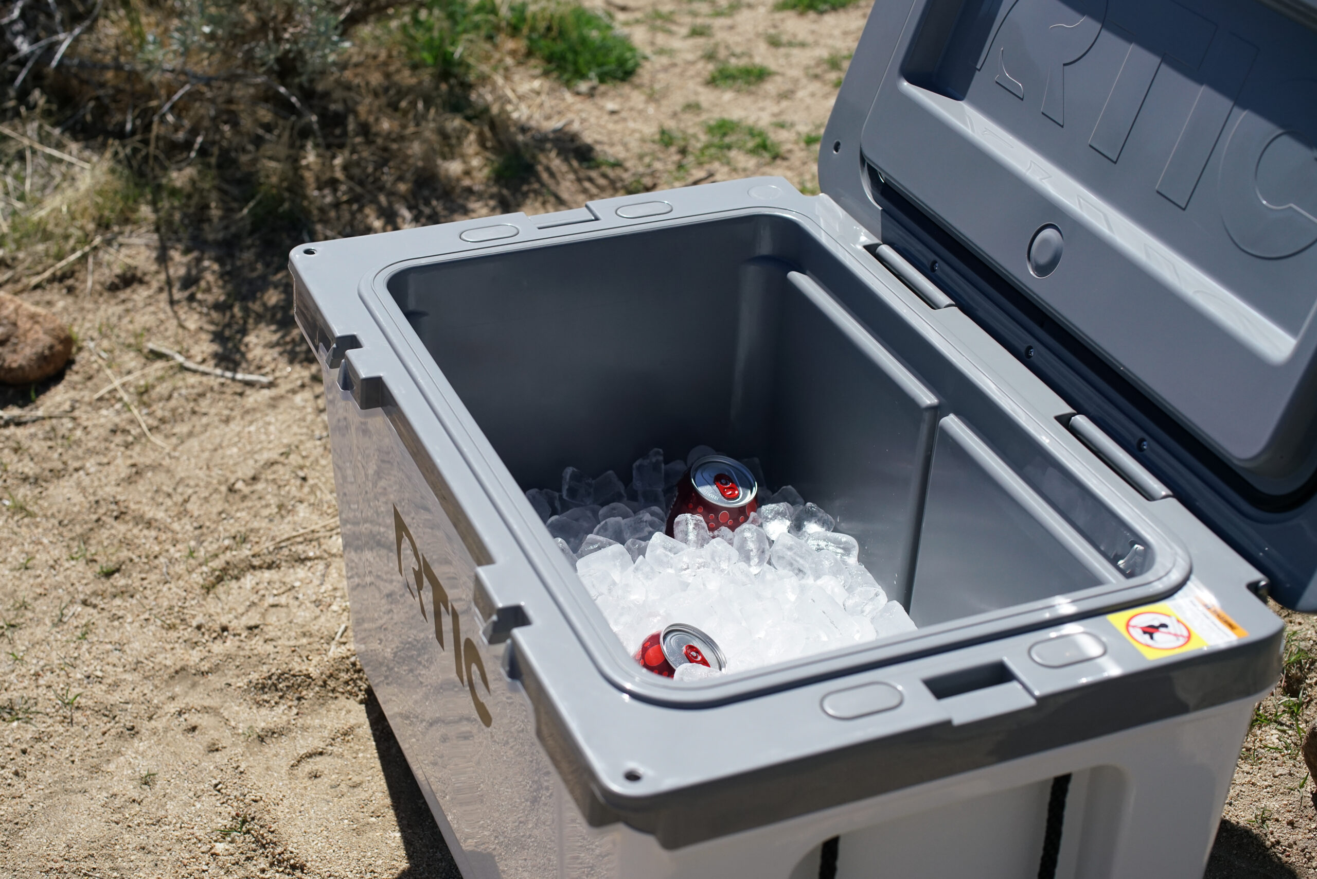 A close up looking into the open RTIC Ultralight 52 cooler. There is ice inside the cooler and a couple canned drinks visible.