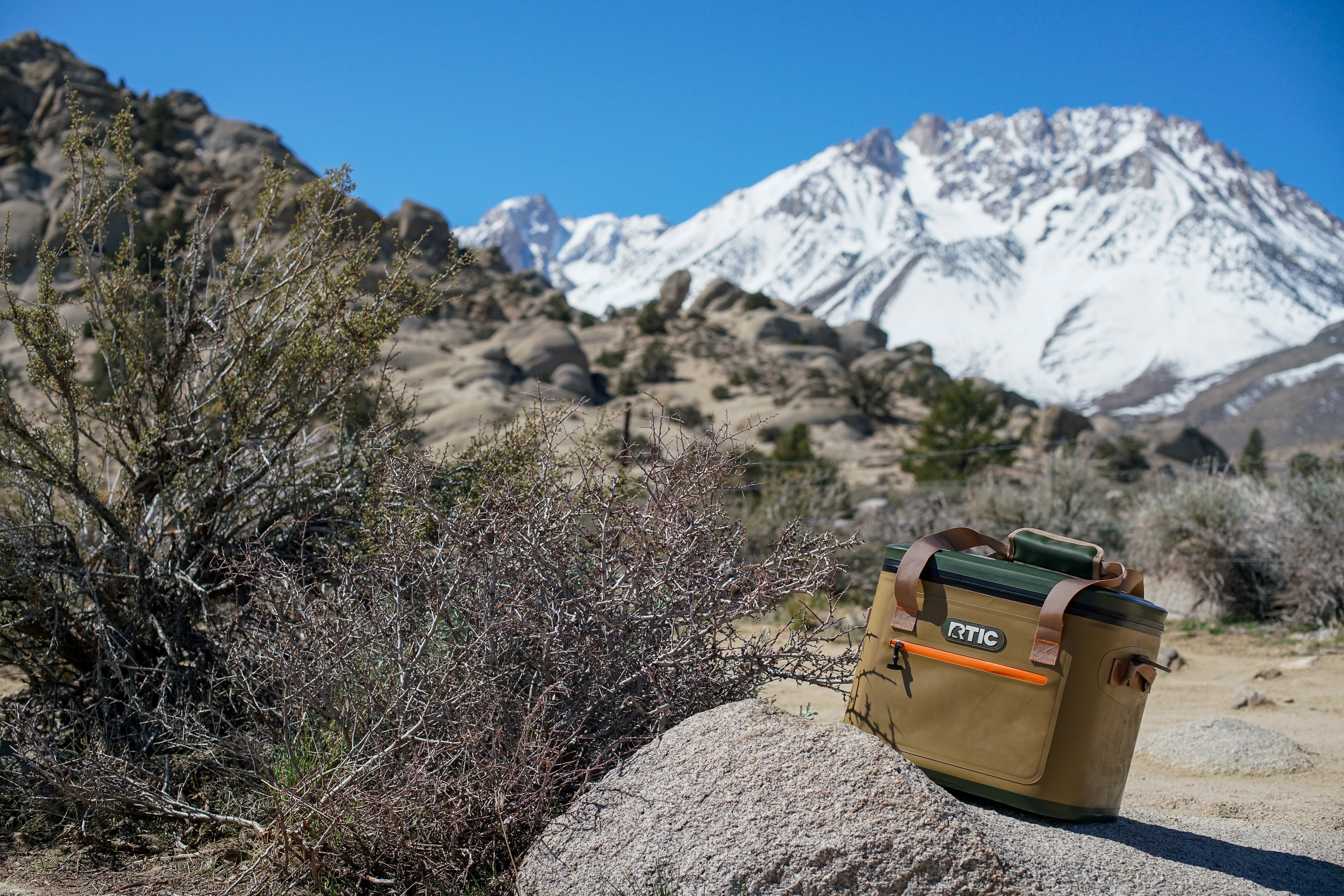 The RTIC Soft Pack leans on top of a rock with boulders and a mountain in the distance.