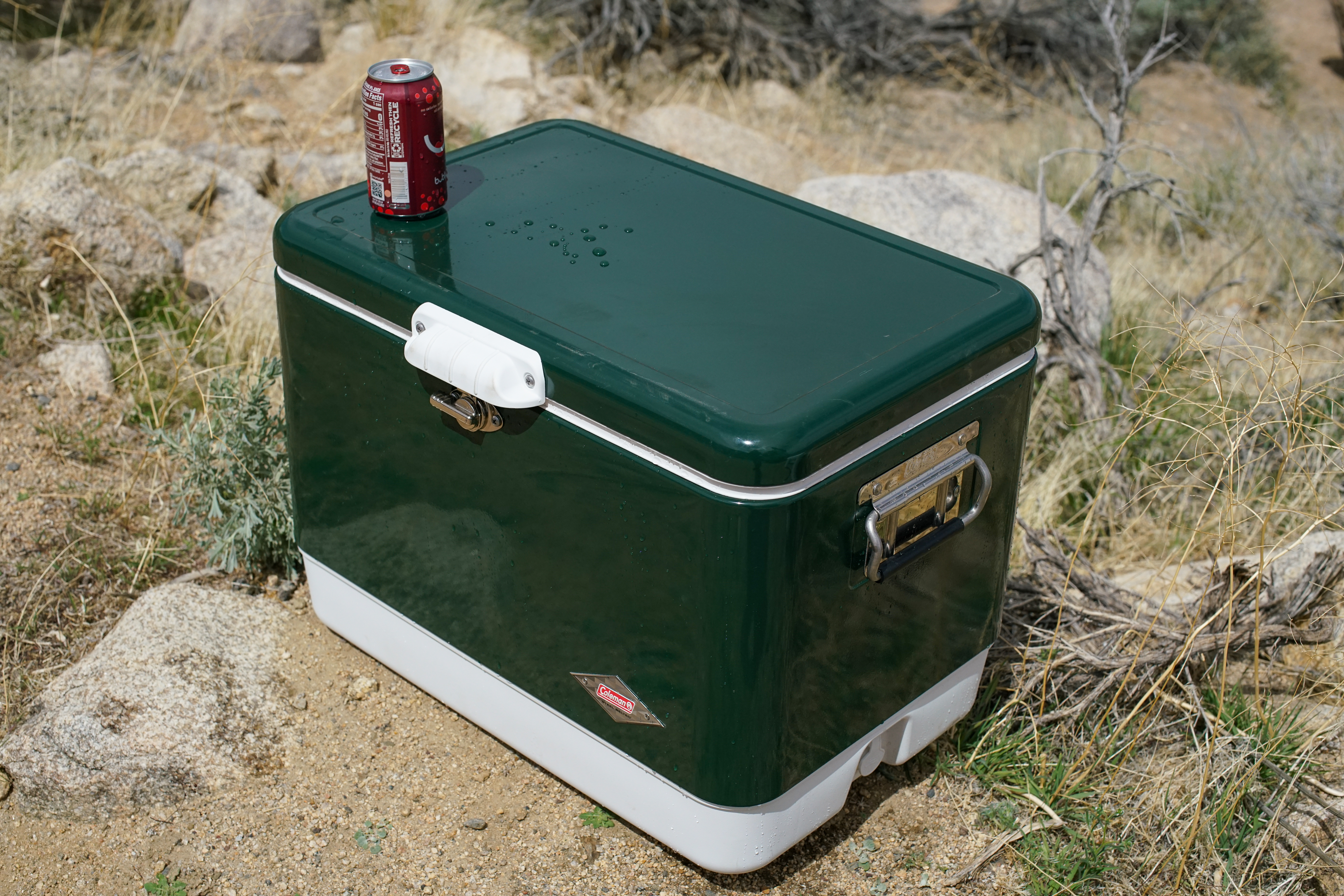 A canned drink sits on top of the Coleman Steel Belted cooler, which sits on the ground.