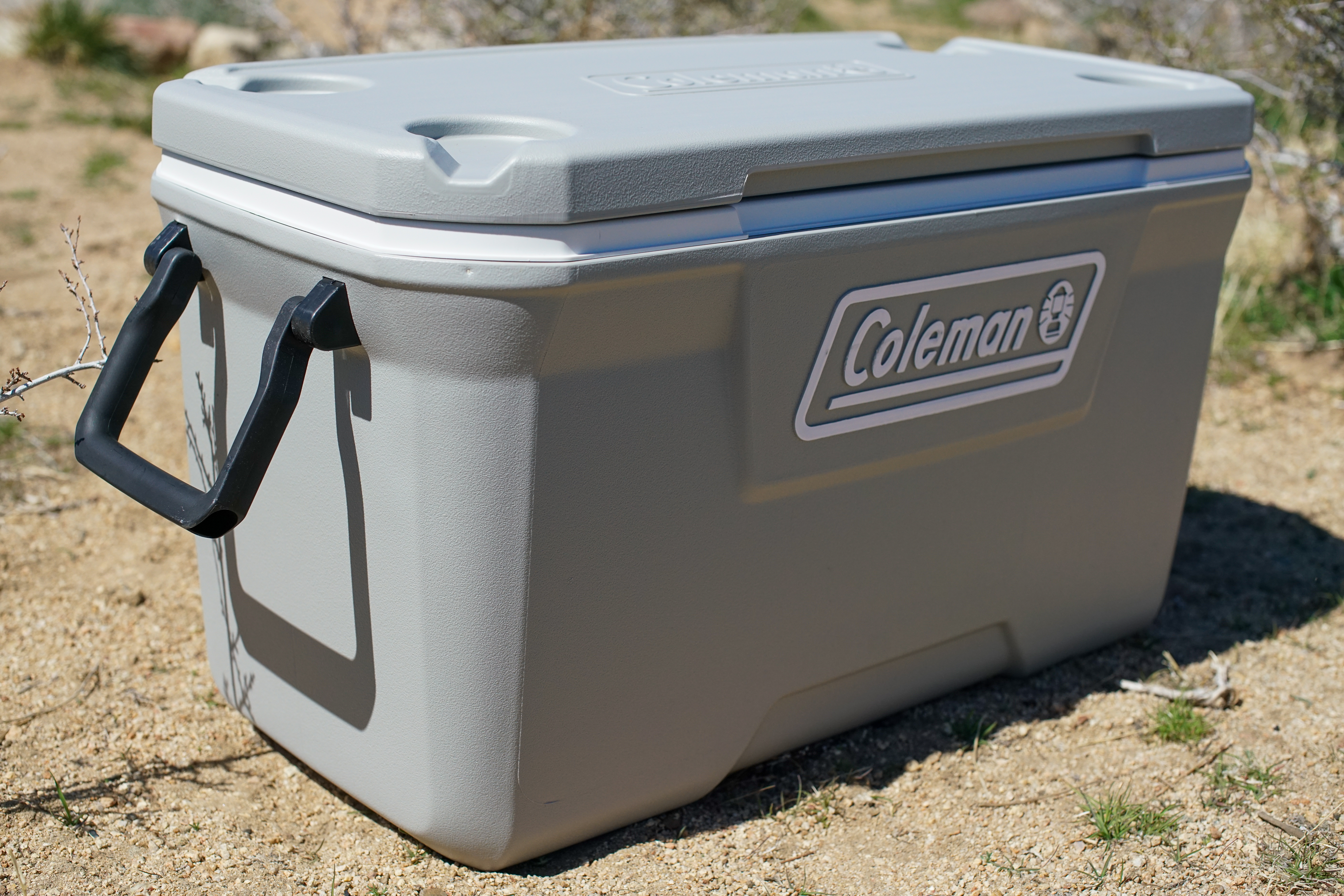 A slightly canted view of the Coleman 316 Series 70QT cooler sitting on the ground.