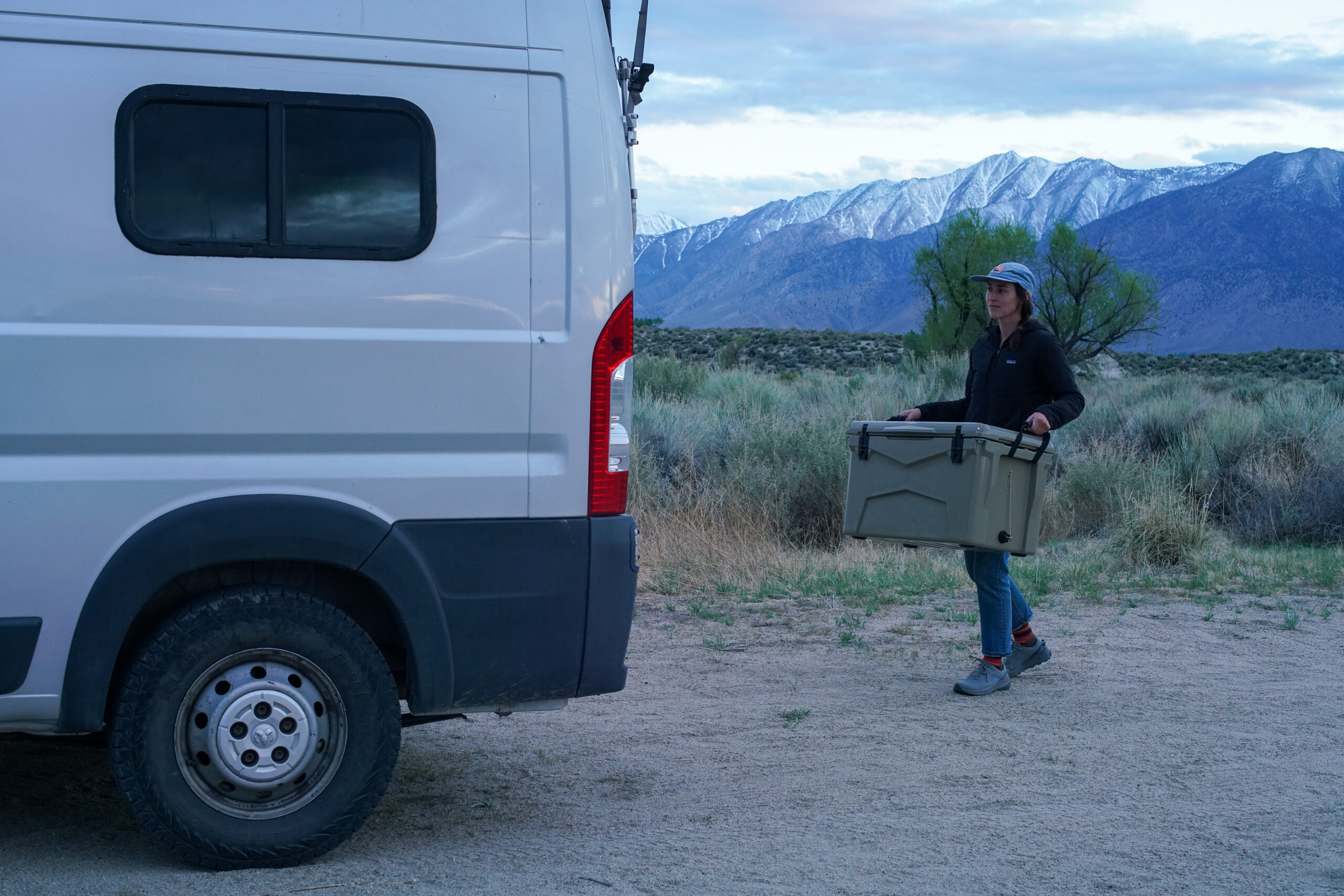 A person carries the XSpec 60QT cooler towards a silver van.