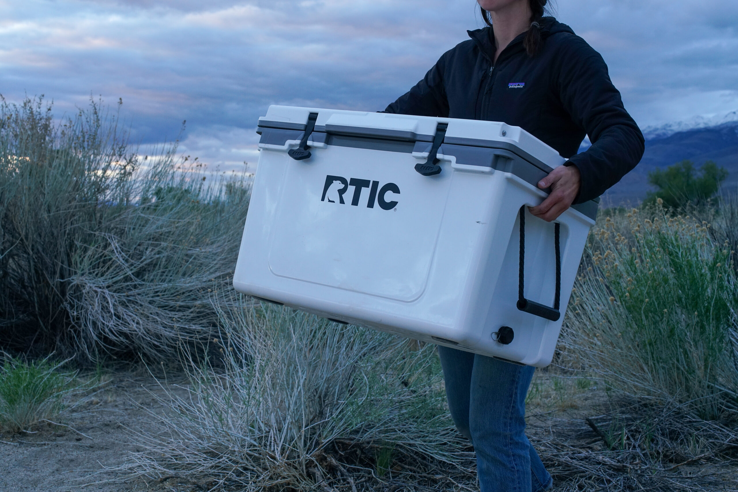 A close up of a person carrying the RTIC Ultralight 52 cooler by its built-in molded side handles.