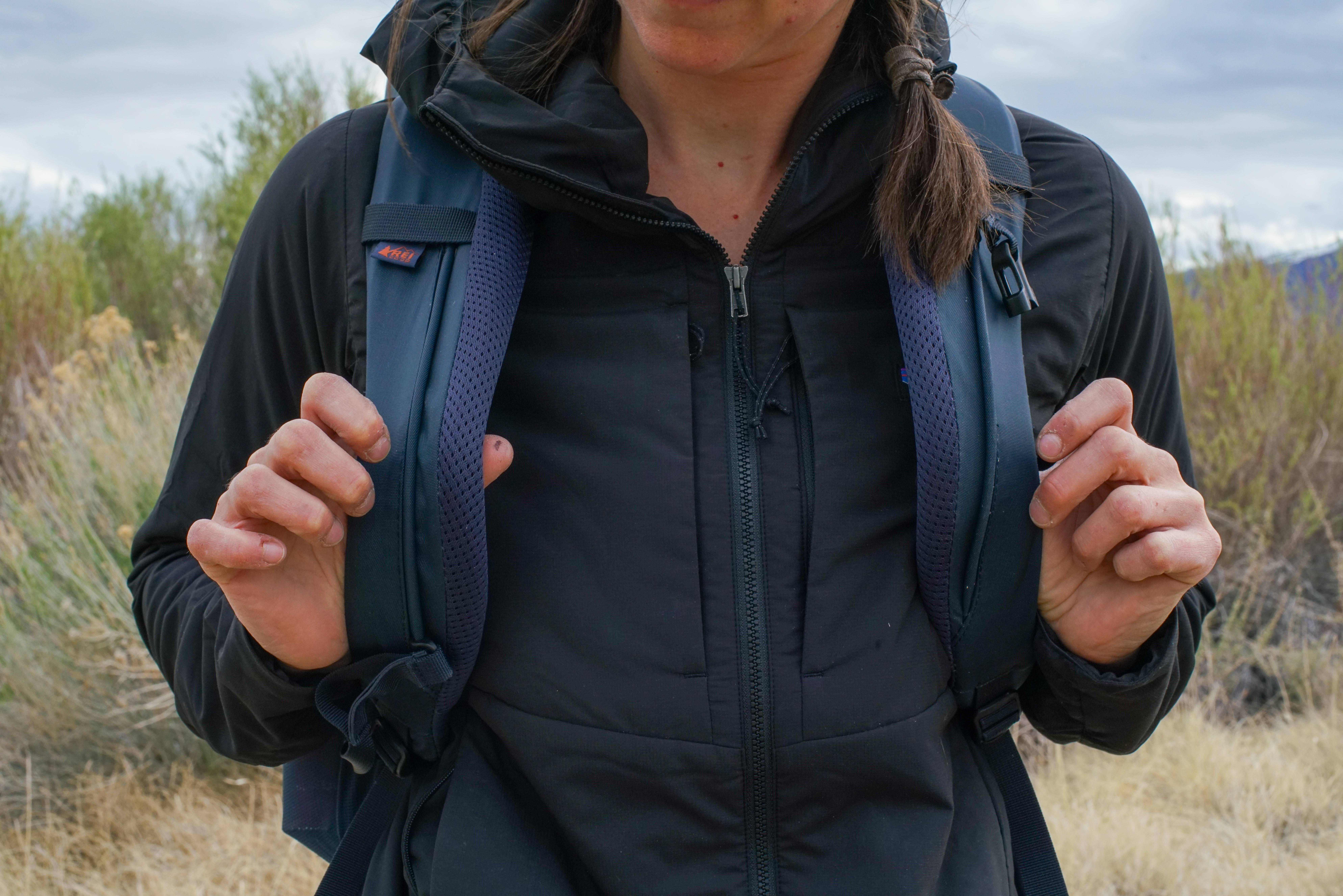 A close up of a person tugging on the straps of the REI Cool Trail Split Pack. Their face is not visible.