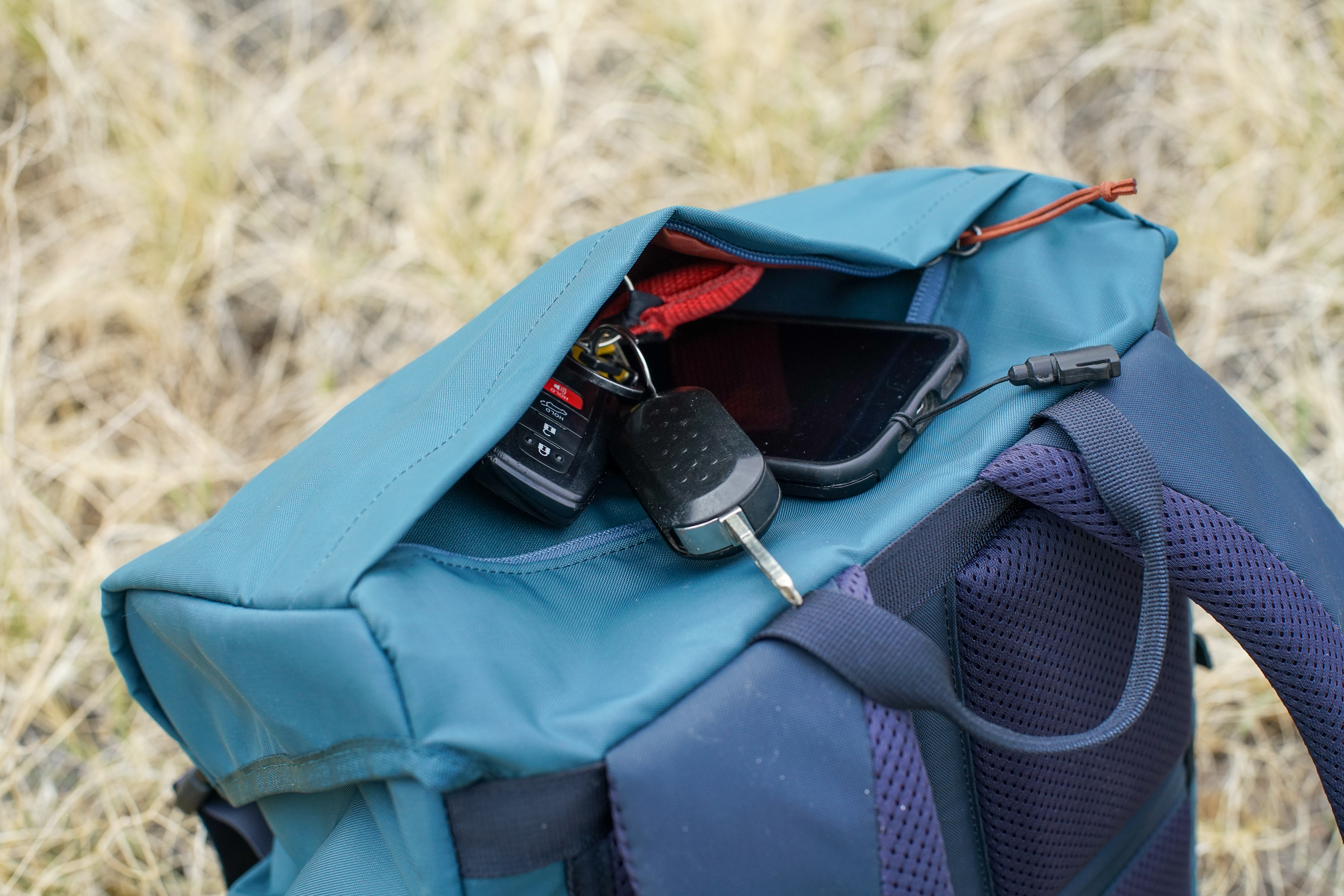 A close up of the top lid pocket on the REI Cool Trail Split Pack. Some car keys and a phone stick out of the partially unzipped pocket.