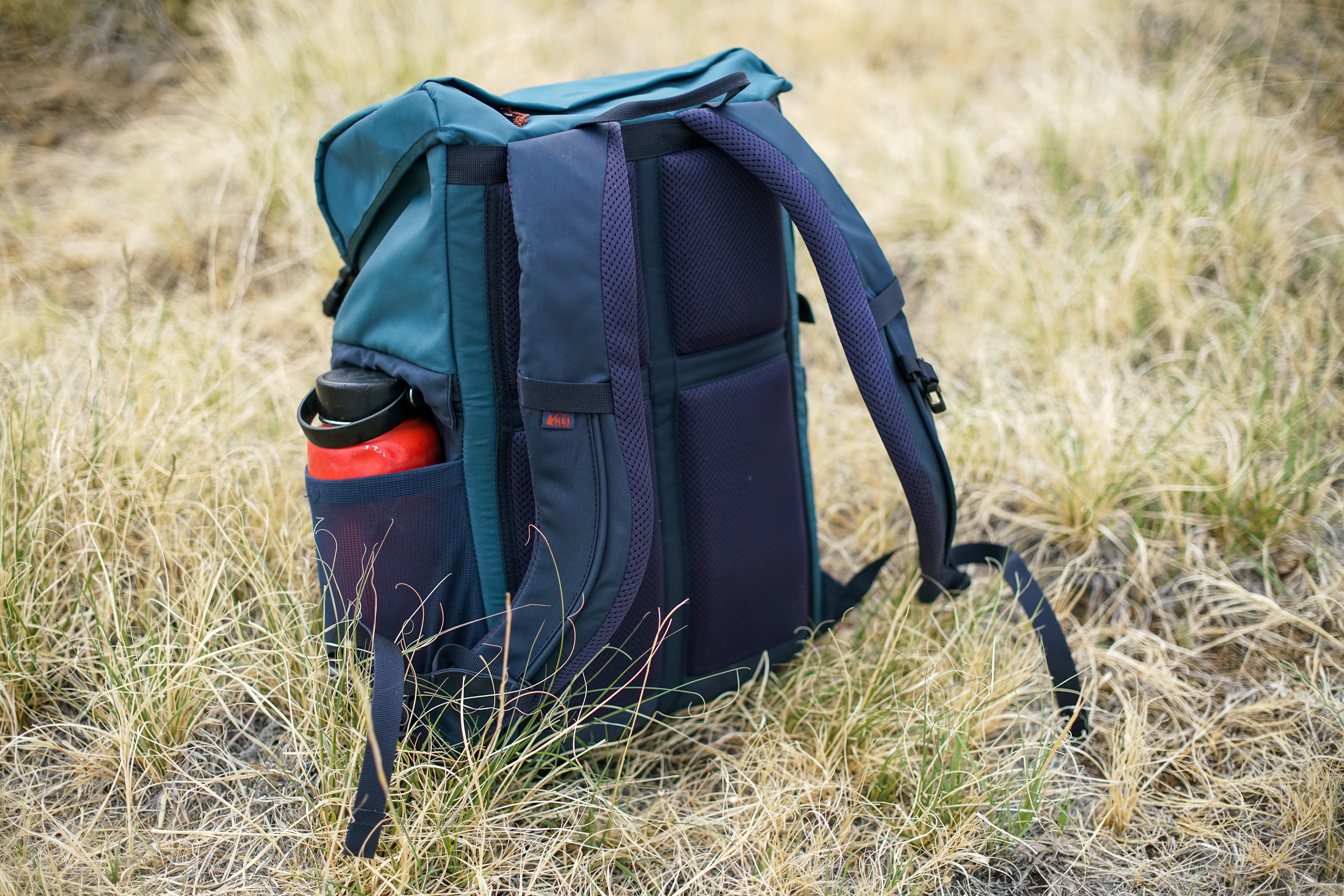 The REI Cool Trail Split Pack sits upright on grassy ground.