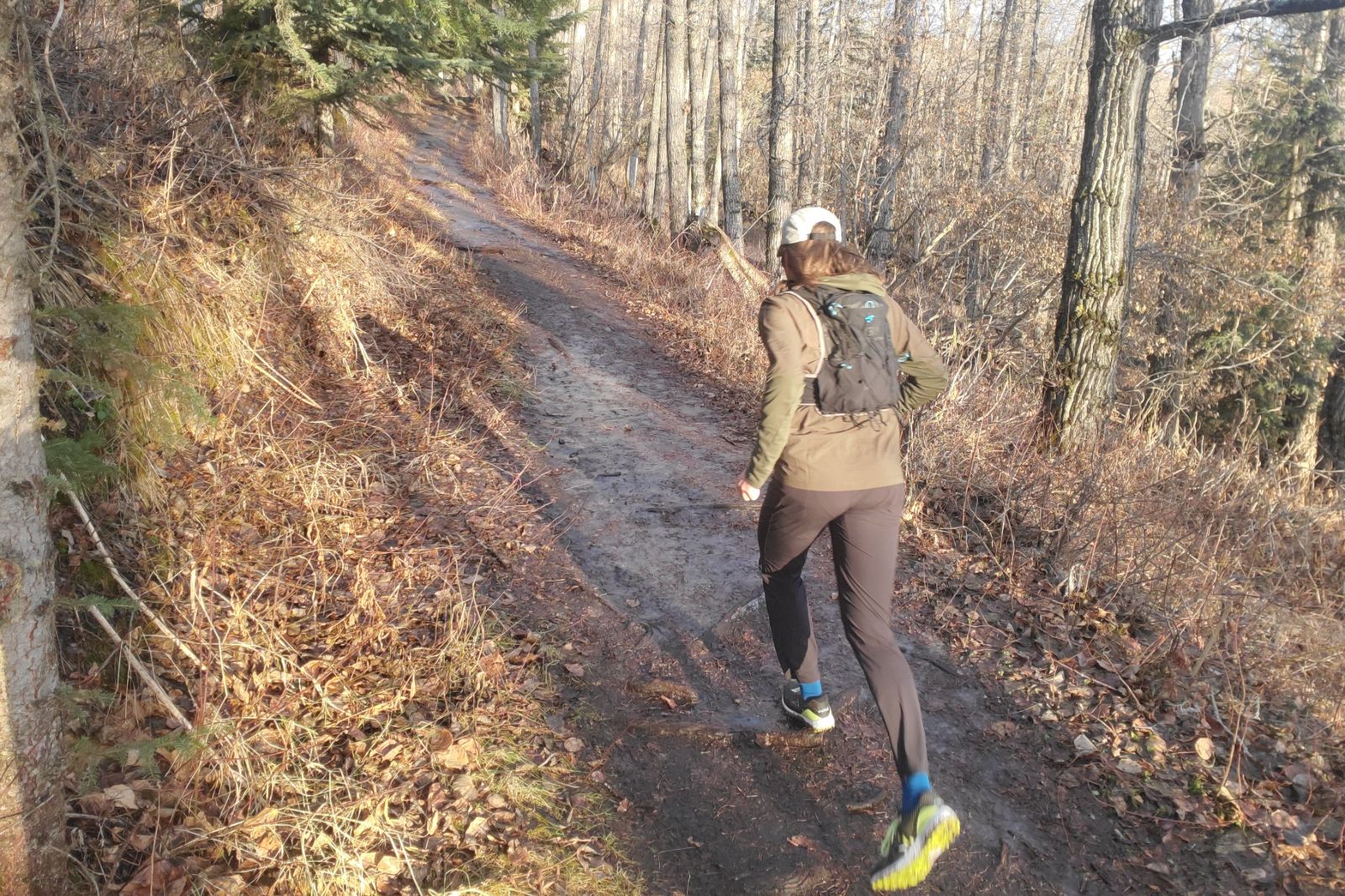 A man runs away from the camera down a muddy trail wearing a green jacket.