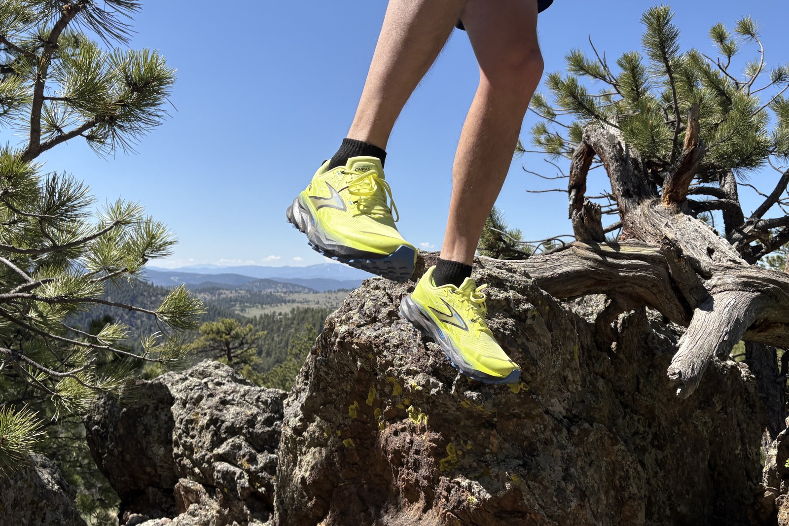 A knees-down photo of a man jumping off of a rock on a blue bird day with mountains in the background.
