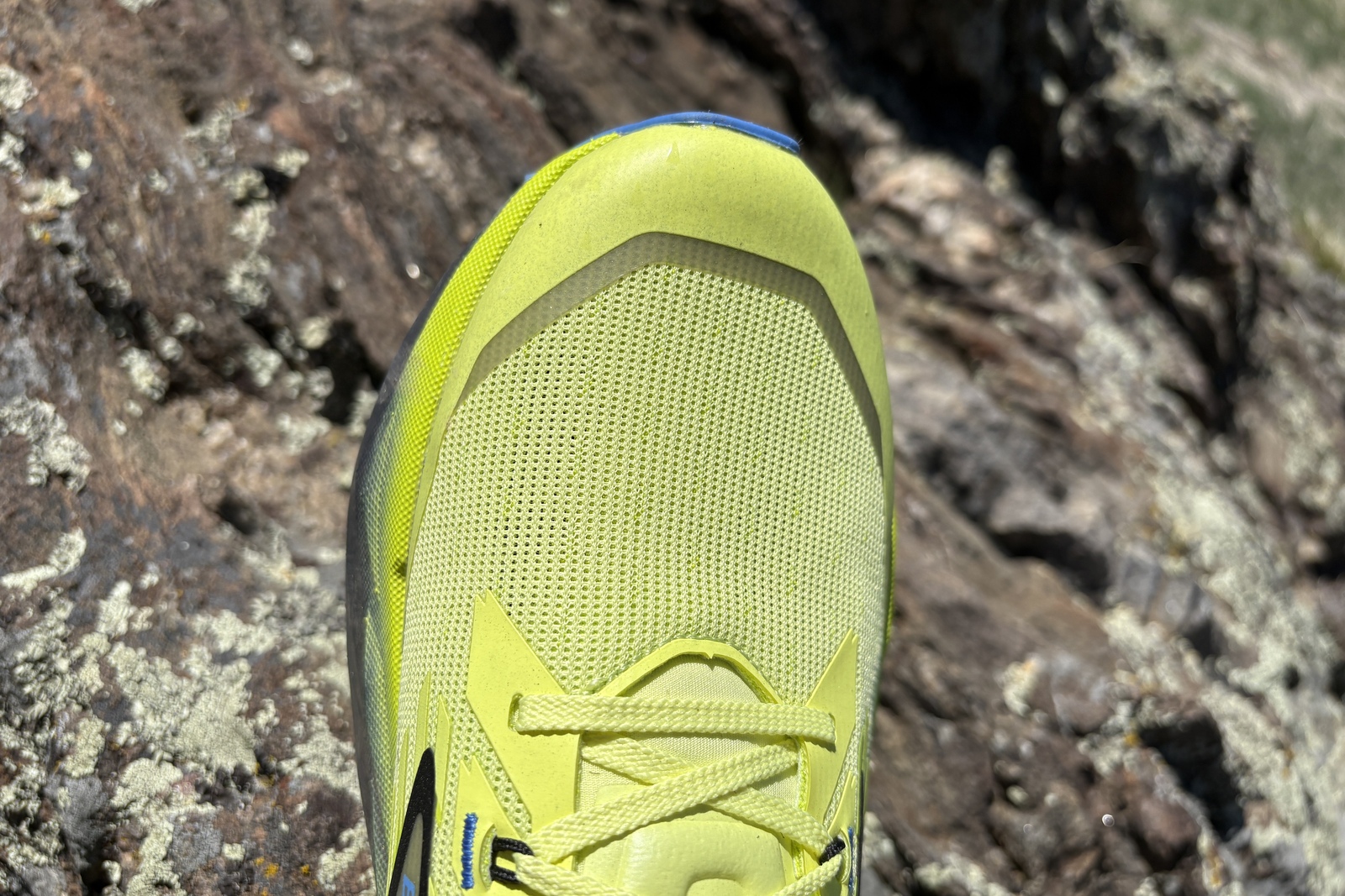 The front end of a neon yellow running shoe hanging over a rock.