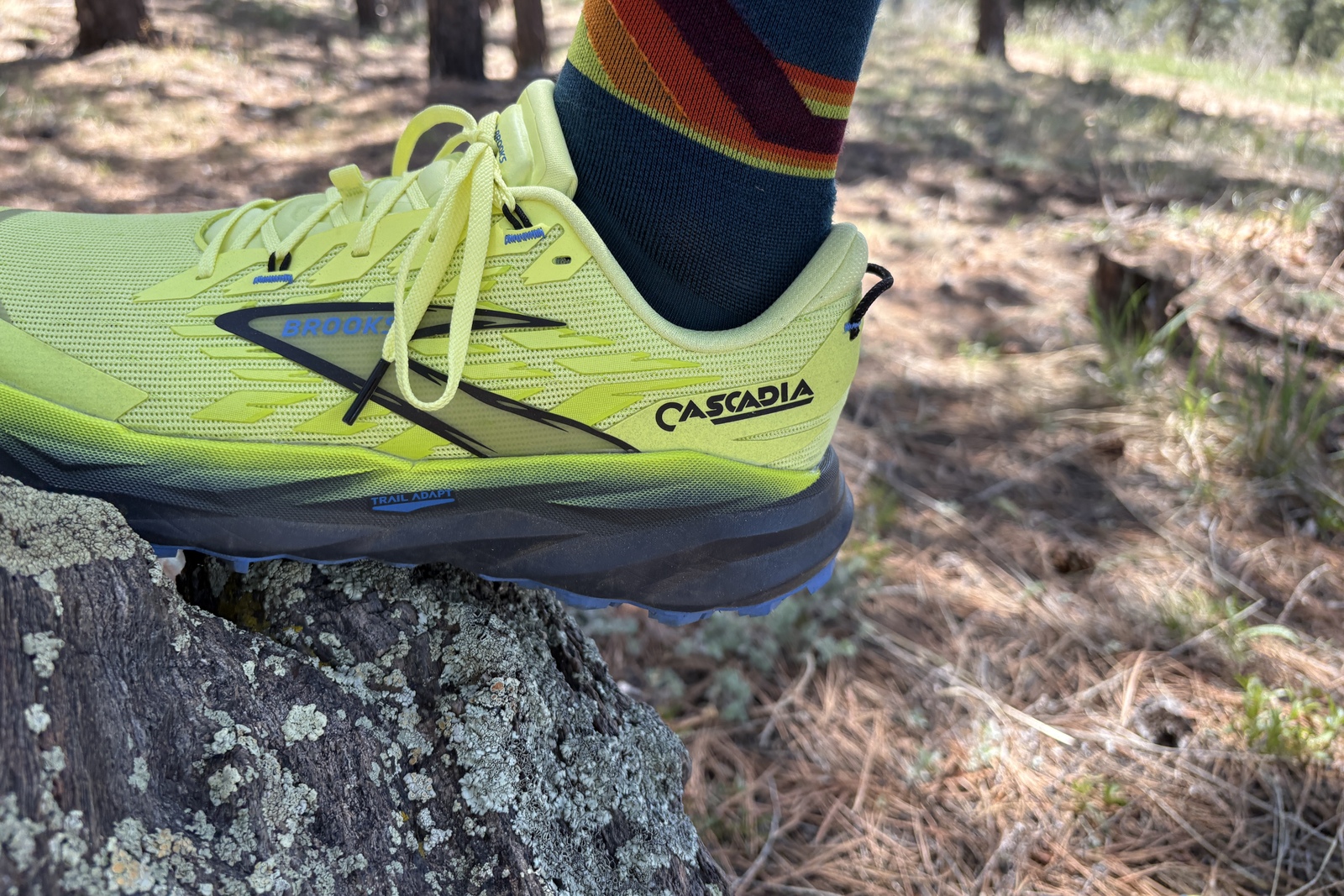 A closeup of a neon yellow running shoe with runner's foot resting on a rock.