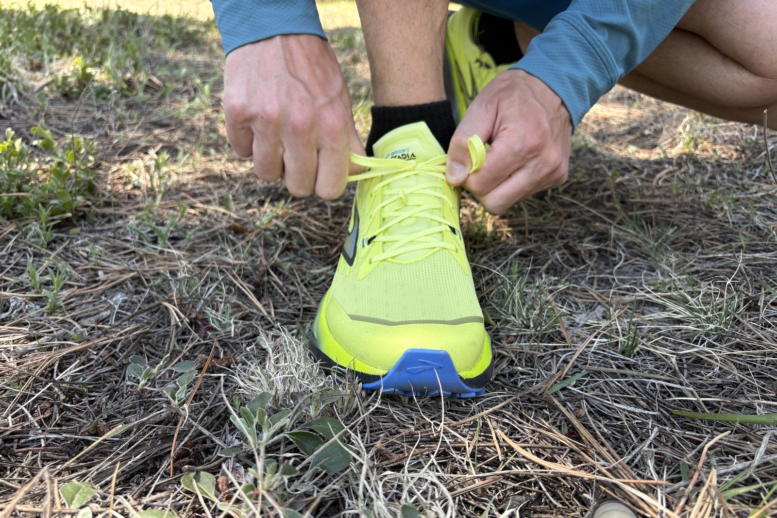A man kneels down to tie the laces of a neon yellow shoe.