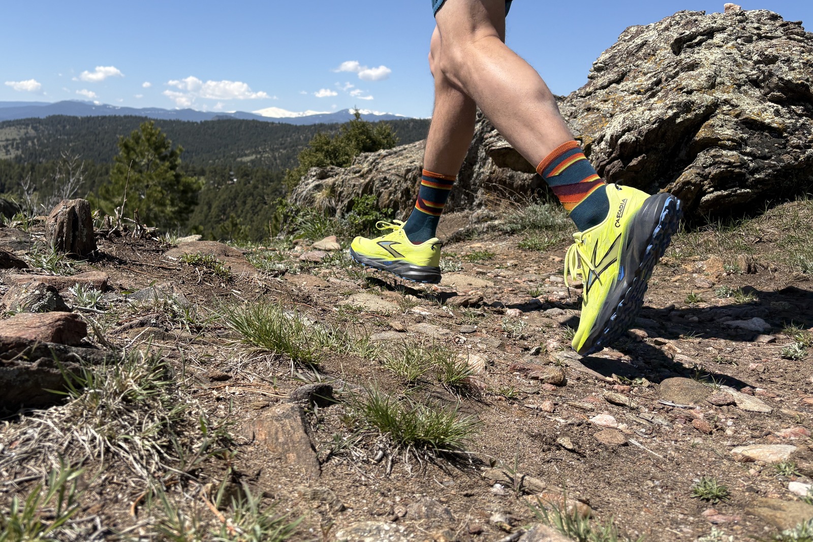 A person running on a hiking trail with neon yellow shoes and mountains in the distance.