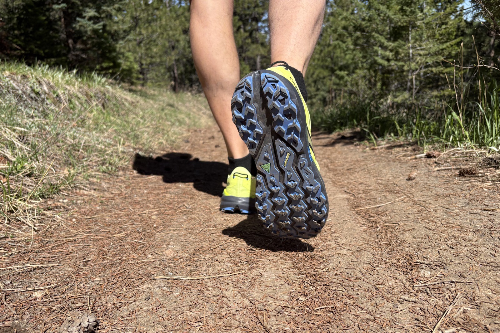 The feet of a man waking on a hiking trail with the underside of his right foot showing the shoe's traction.