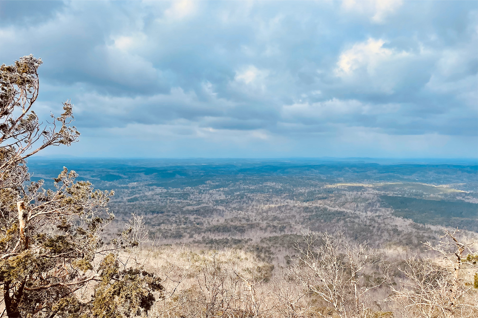 The picture is taken from the edge of an overlook on a ridge. The lands below are flat and forested.