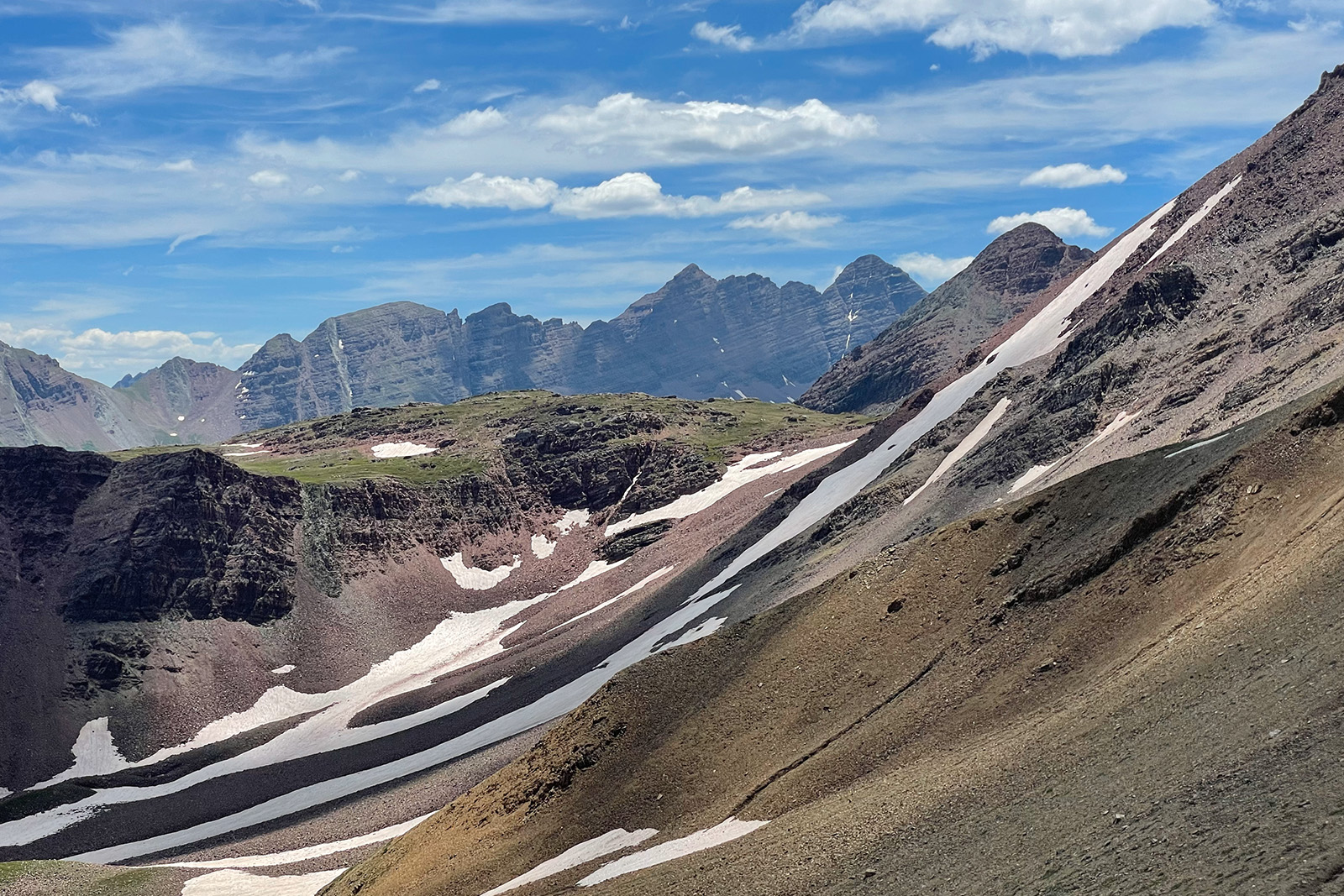 Scree and snow fields make up the foreground of this photo with striated mountains in the distance.