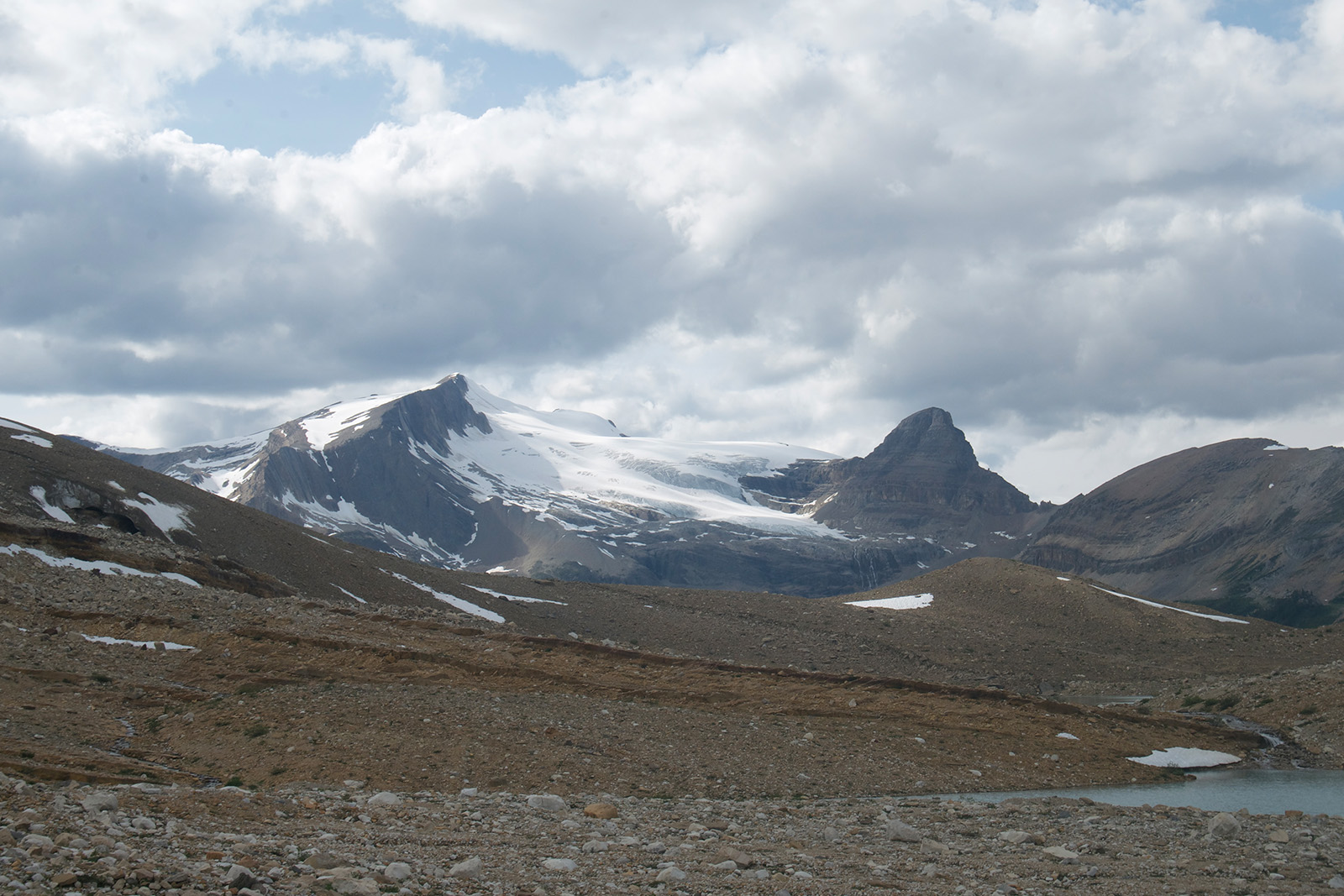 The viewer is standing in a rocky, open area. There is a mountain rising in the distance covered in a glacier.