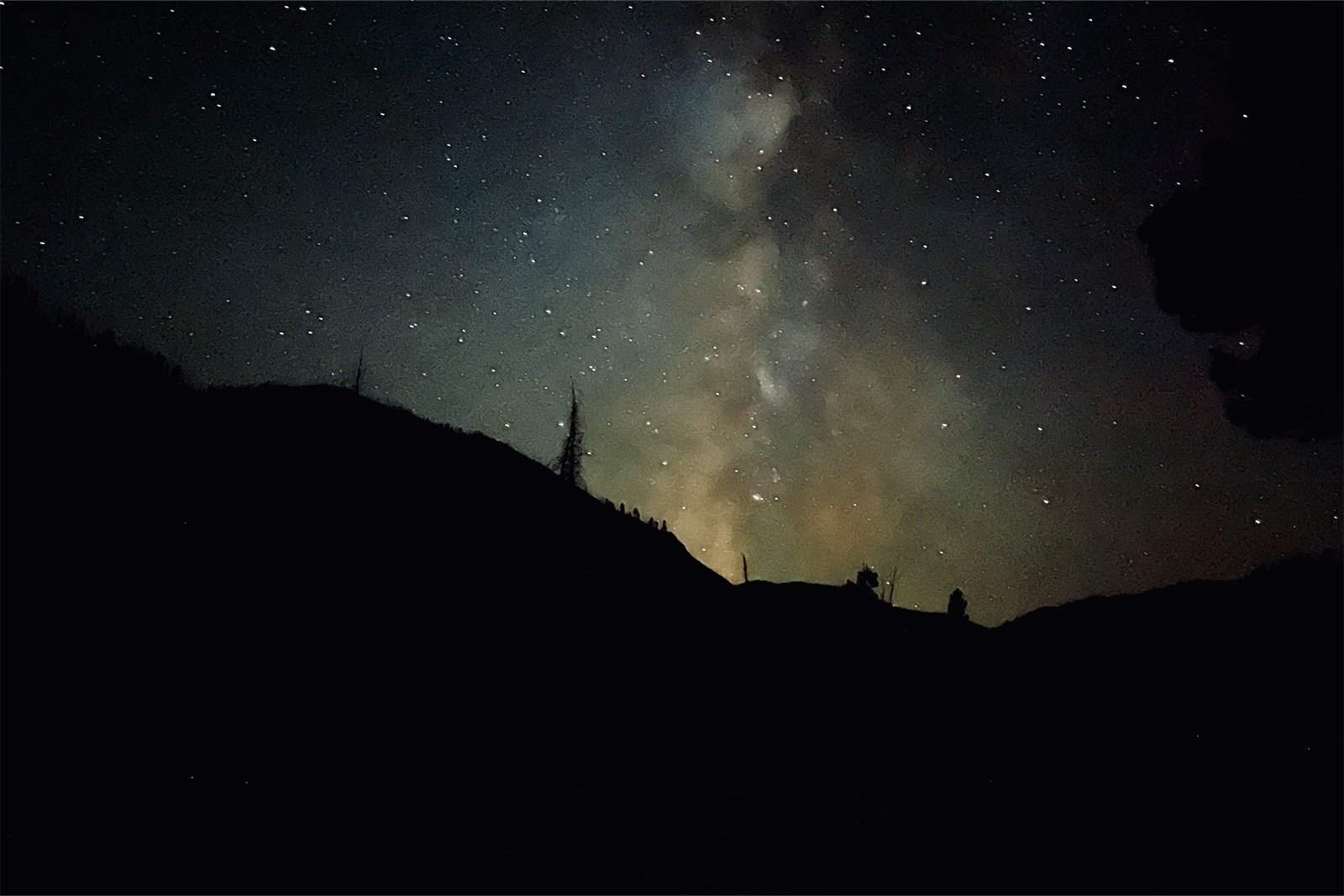 The milky way and stars are visible above a mountain at night.