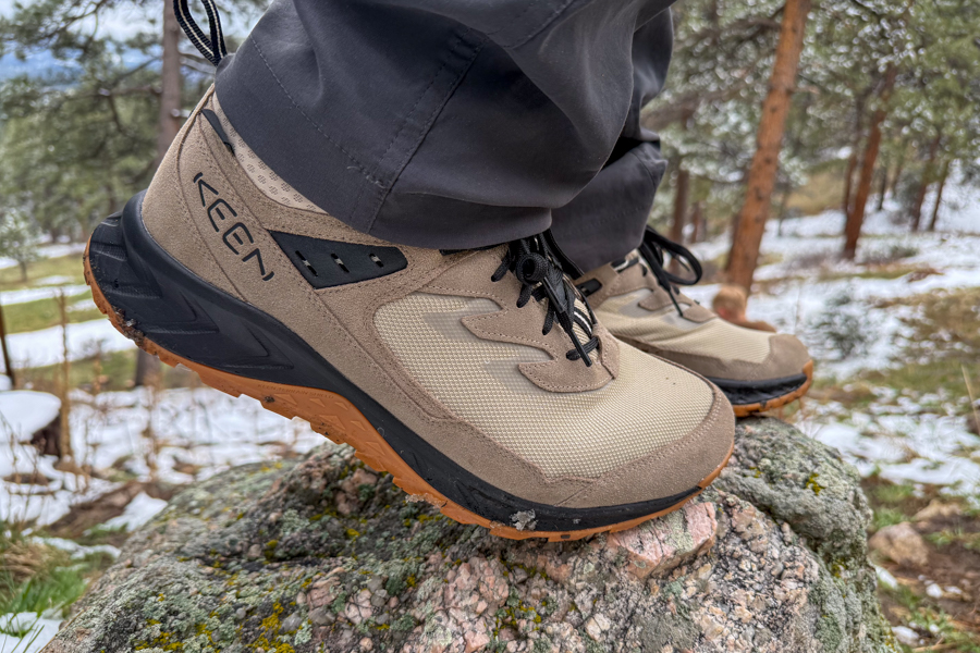 Hiker leaning forward, boots stepping on a snowy rock, highlighting midsole flex.