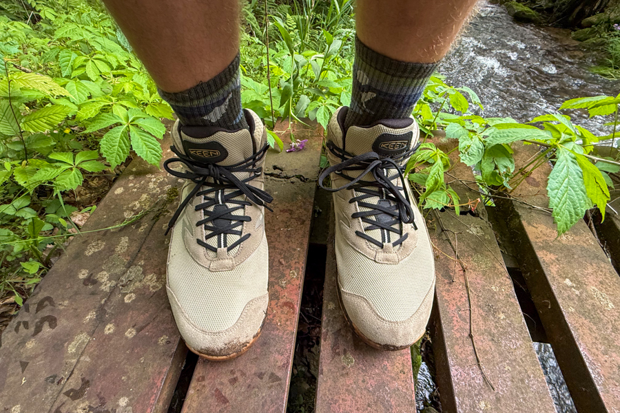 Hiker’s legs and Keen Hightrail Mid boots standing on a narrow wooden bridge.