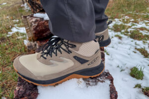 Close-up of boot outsole on snow-covered log, showing mud-clearing lug pattern.