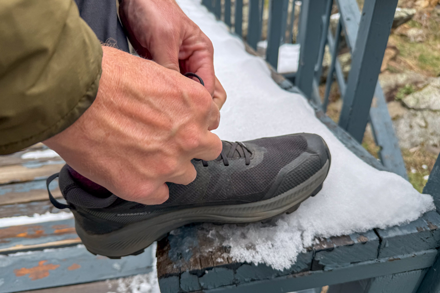 A man ties his shoe on a bench. The bench is covered in snow.