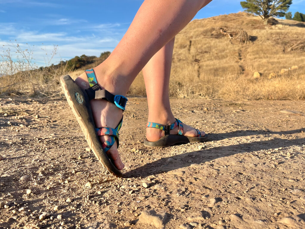A woman walking along a dirt trail wearing Chaco Z/1 Classic hiking sandals.