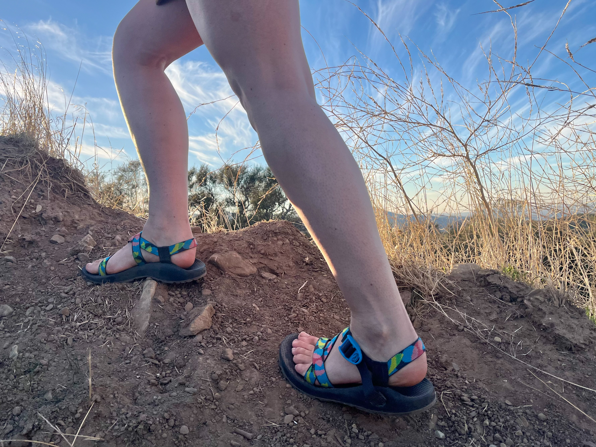 A woman climbing up a slippery dirt slope wearing Chaco Z/1 Classic hiking sandals.