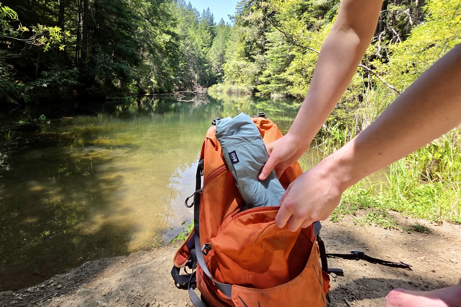 Women packing up the rolled up REI Trailmade shorts into her day pack.