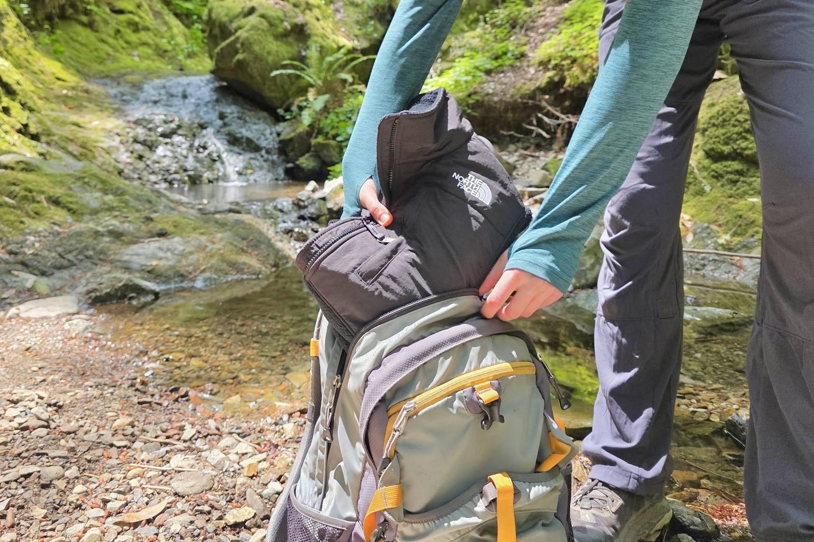 Woman stows away her folded fleece jacket in her day pack.