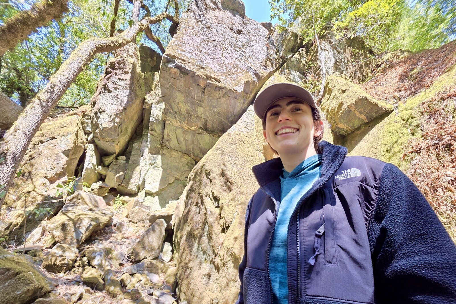 Woman stand before a rock outcropping, modeling the chest of the North Face fleece.
