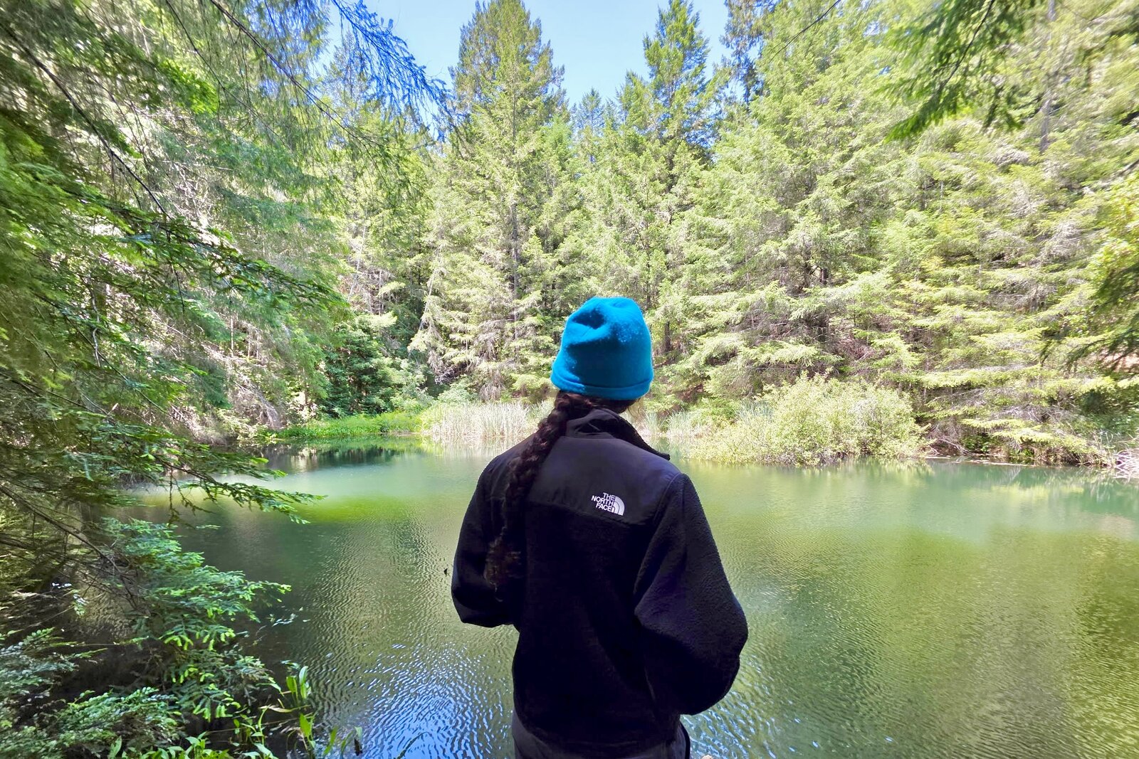 Woman facing a lake, showing the back of the North Face Retro Denali fleece.