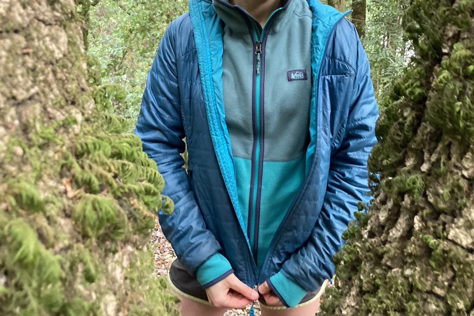 Close up of a woman zipping up a puffy jacket over her REI fleece.