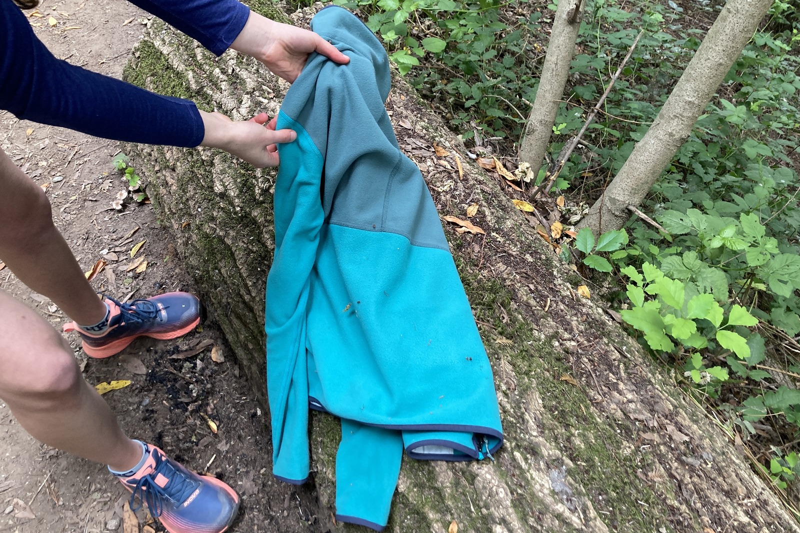 A fleece jacket lays on a mossy log with some debris clinging to the fabric.