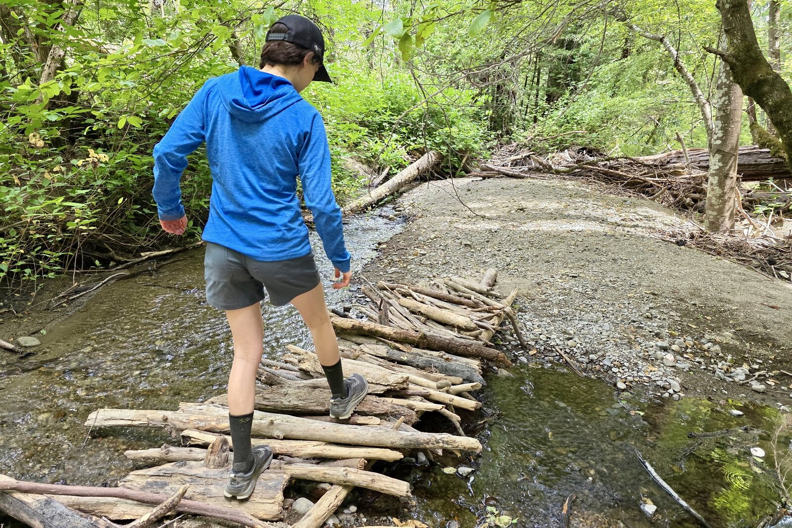 Woman walks across a wooden bridge over a creek.
