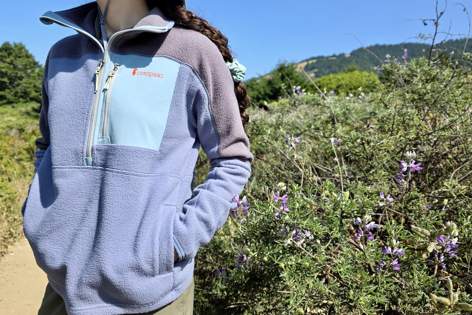 A woman stands next to a blooming lupine bush with her hands in the pocket of her fleece.
