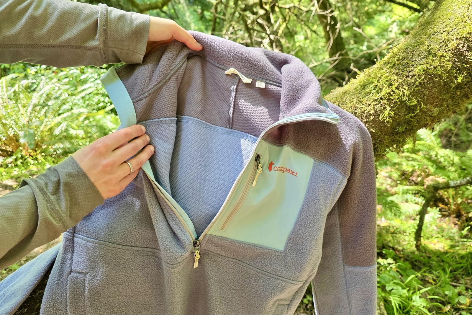 A woman holds up her fleece sweater, showing the difference in material used on the inside vs the outside of the jacket.