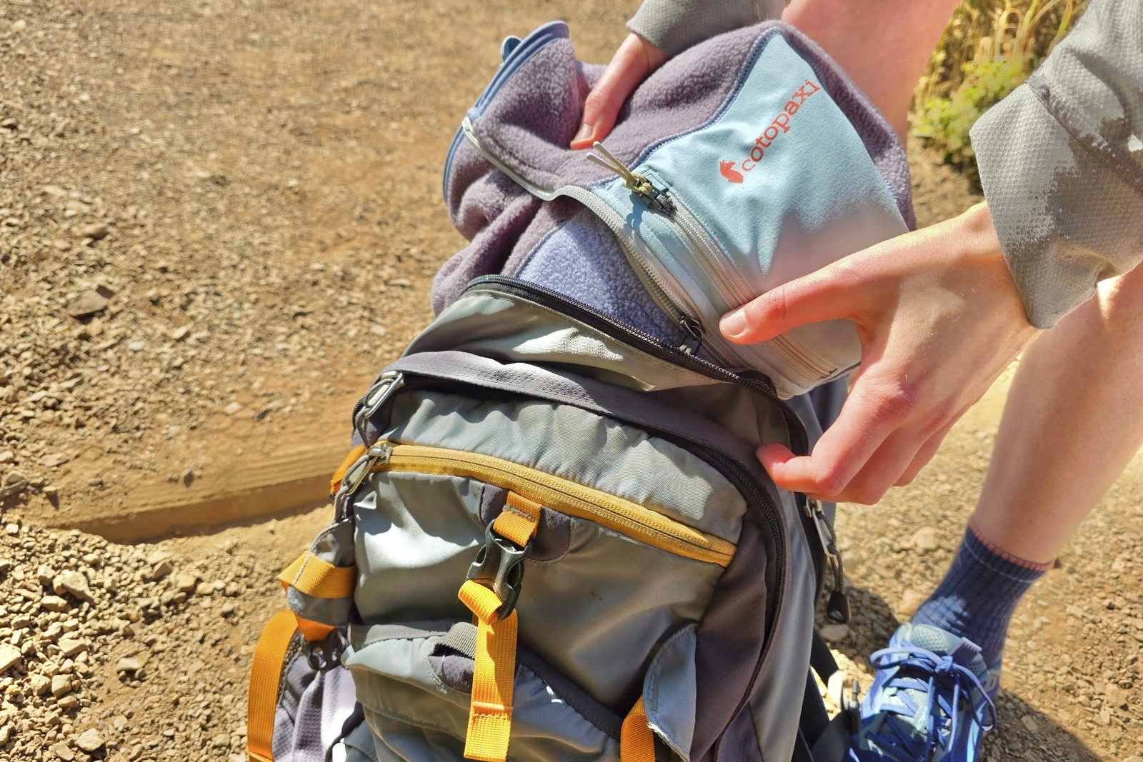 A woman packs a folded fleece sweater into her backpack.