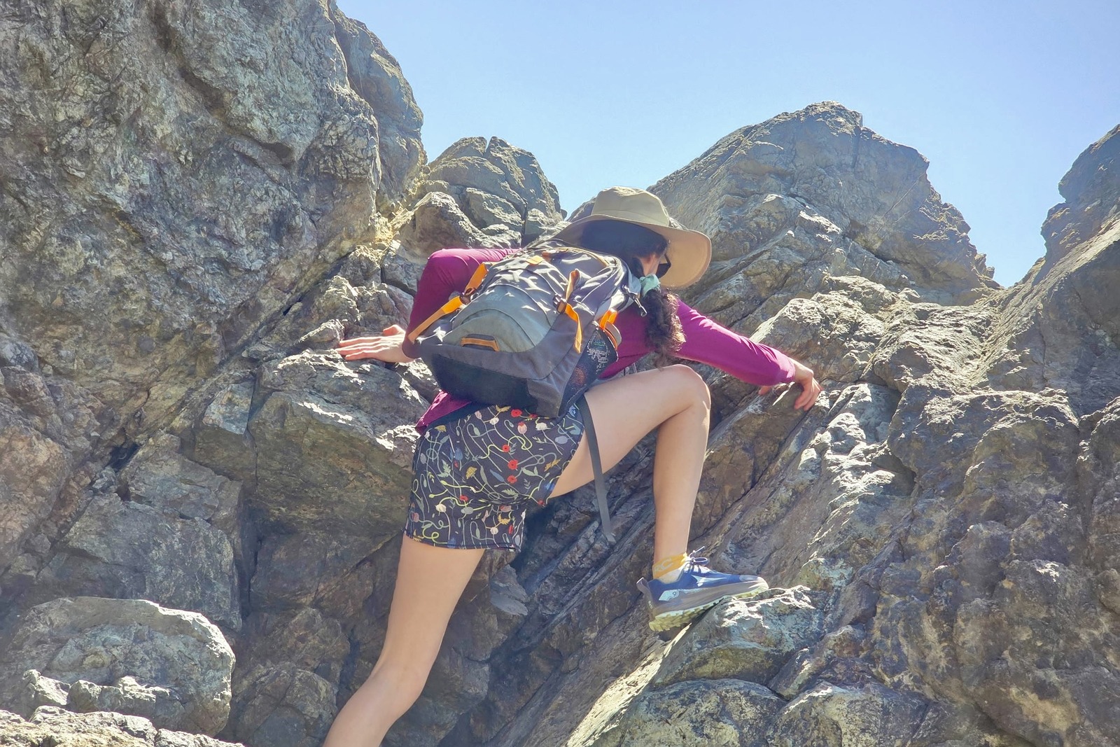 A woman scrambles up a rock face, taking a large step.