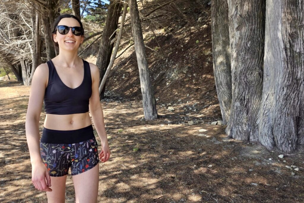 A woman walks through a forest in her sports bra and Oiselle shorts.