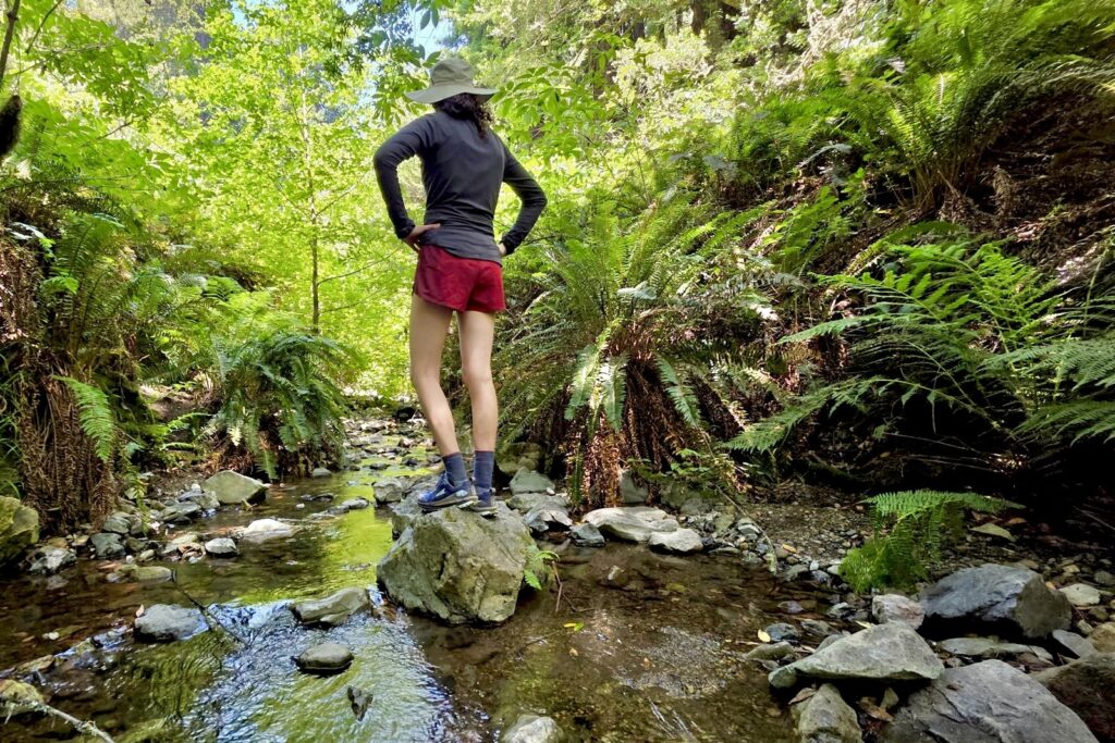 A woman stands on a rock in the middle of the creek.