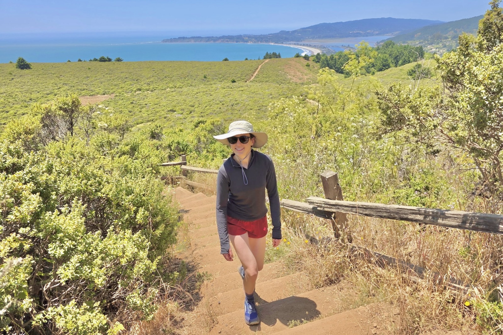 A woman hikes along an exposed trail with the beach in the background.