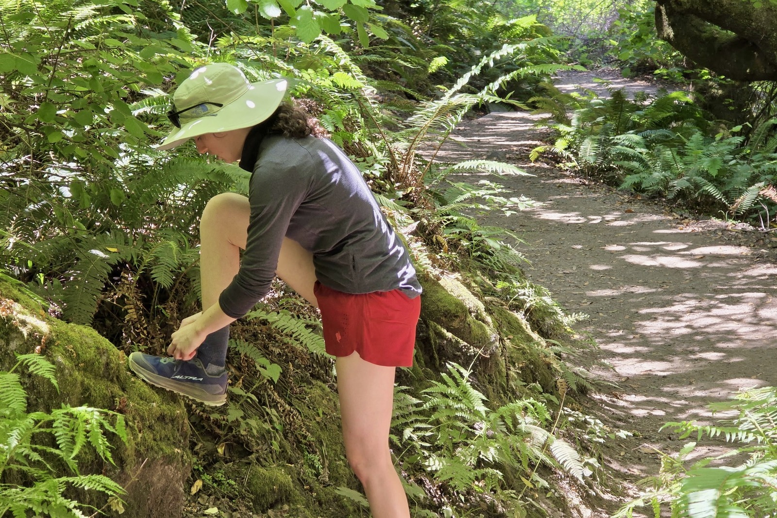 A woman lifts her leg up onto a high rock to tie her shoe.