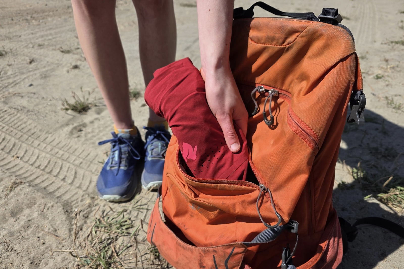 A woman packs up her rolled up shorts into her daypack.