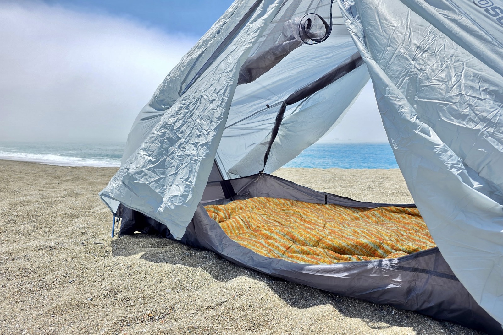 A Kelty blanket is laid out inside of a 2-person tent at the beach.