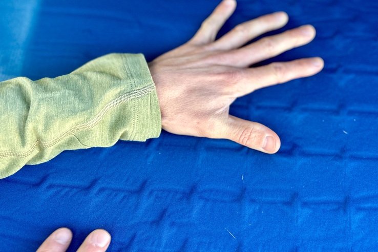Close up image of a hand on the surface of a camping mattress with fingers spread wide.