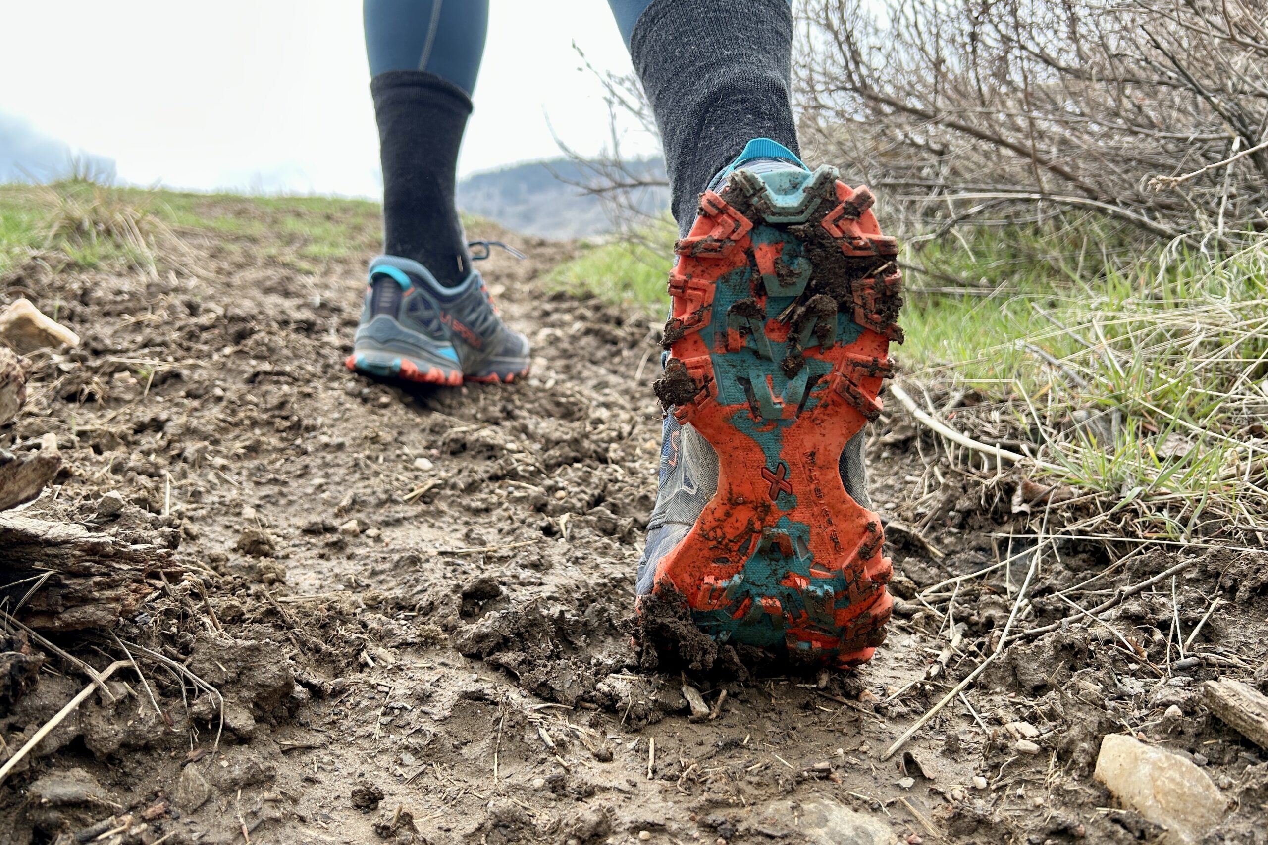 Underside traction view of a trail runner in a muddy section of trail.